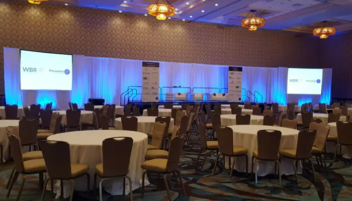 Corporate event production setup in San Diego featuring a professional stage, LED screens, lighting, and banquet seating for a business conference.