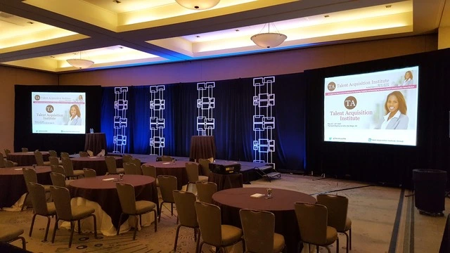 Professional corporate event lighting setup featuring stage truss lighting, projection screens, and conference seating for a San Diego general session presentation.
