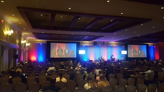 Professional virtual conference production in San Diego featuring keynote presentations, multiple projection screens, classroom seating, and a corporate audience.